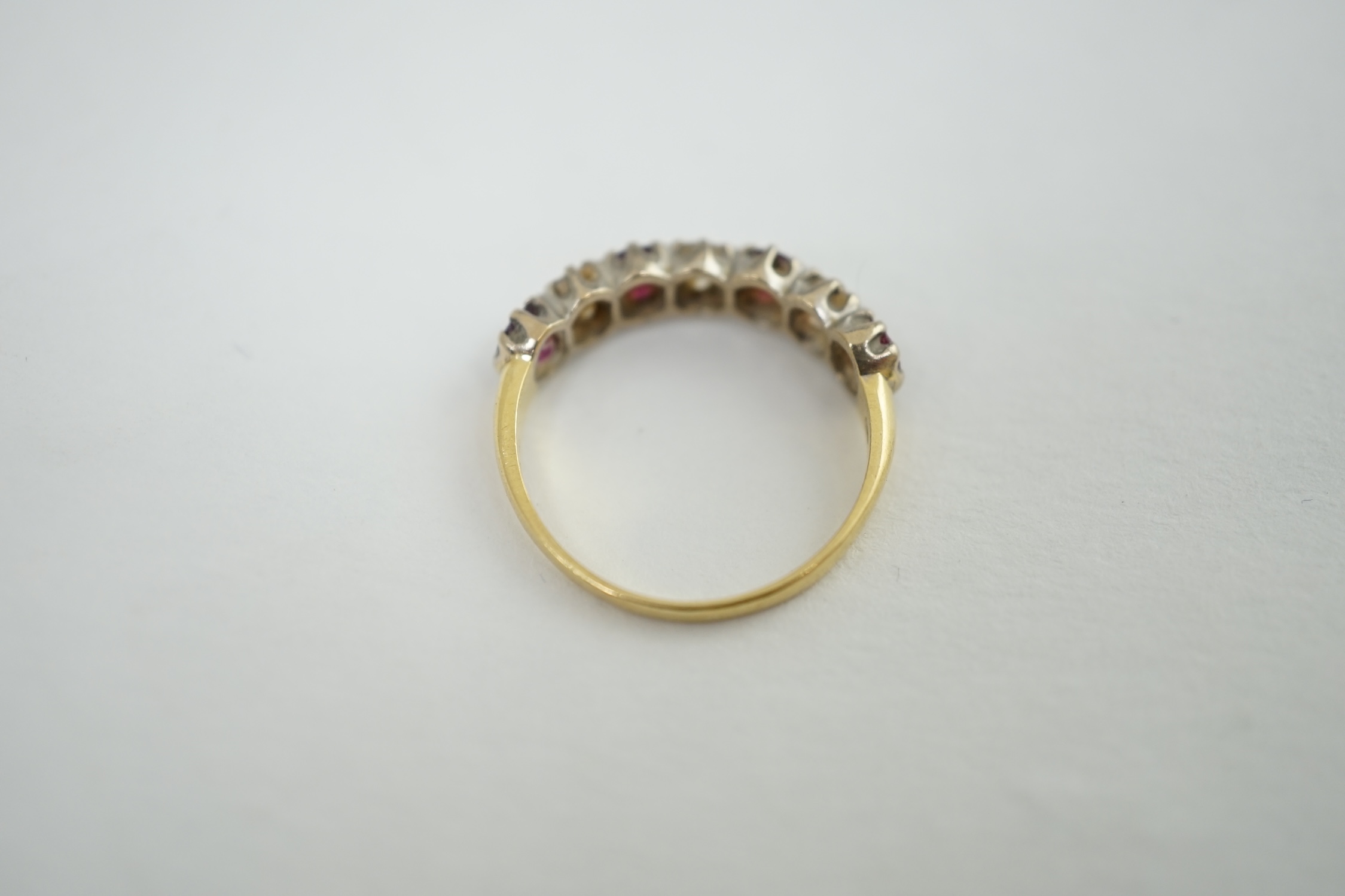 An 18ct yellow and white gold three stone diamond and four stone ruby set half hoop ring